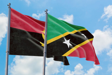 Saint Kitts And Nevis and Angola flags waving in the wind against white cloudy blue sky together. Diplomacy concept, international relations.