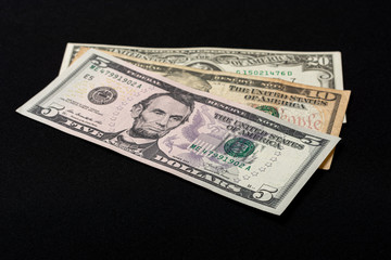 Five, ten and twenty dollar bills lie on a black background.