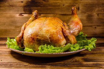 Plate with roasted whole chicken and lettuce leaves on a wooden table