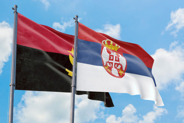 Serbia and Angola flags waving in the wind against white cloudy blue sky together. Diplomacy concept, international relations.