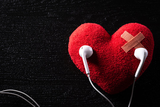 First aid band cushioned plaster strip medical patch glued on red heart with earphone listen to music on wooden background. Heart broken, Love and Valentines day concept.
