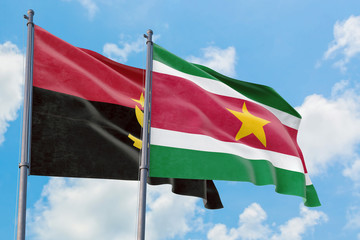 Suriname and Angola flags waving in the wind against white cloudy blue sky together. Diplomacy concept, international relations.