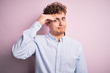 Young blond handsome man with curly hair wearing striped shirt over white background worried and stressed about a problem with hand on forehead, nervous and anxious for crisis