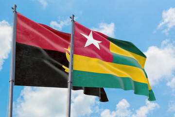 Togo and Angola flags waving in the wind against white cloudy blue sky together. Diplomacy concept, international relations.