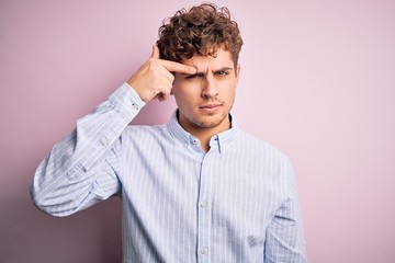Young blond handsome man with curly hair wearing striped shirt over white background pointing...
