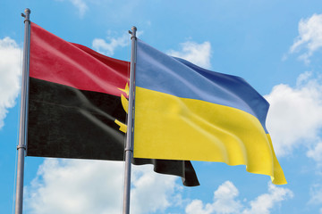 Ukraine and Angola flags waving in the wind against white cloudy blue sky together. Diplomacy concept, international relations.