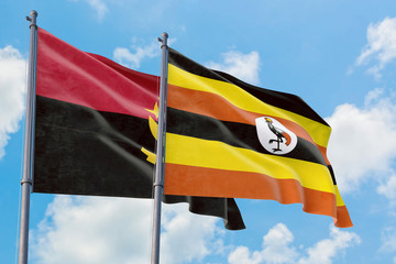 Uganda and Angola flags waving in the wind against white cloudy blue sky together. Diplomacy concept, international relations.