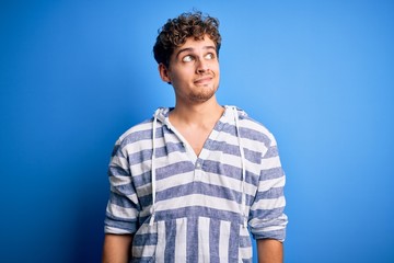 Young blond handsome man with curly hair wearing casual striped sweatshirt smiling looking to the side and staring away thinking.