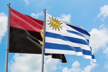 Uruguay and Angola flags waving in the wind against white cloudy blue sky together. Diplomacy concept, international relations.
