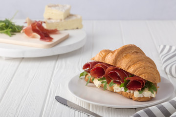 Fresh croissant sandwich with ham, cheese and arugula on white wooden table. Served with Coffee, cheese, ham, orange juice, jam. Fresh French Baked Croissants. Free space for text.