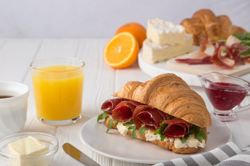 Fresh croissant sandwich with ham, cheese and arugula on white wooden table. Served with Coffee, cheese, ham, orange juice, jam. Fresh French Baked Croissants. Free space for text. 