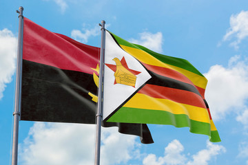 Zimbabwe and Angola flags waving in the wind against white cloudy blue sky together. Diplomacy concept, international relations.