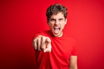 Young blond handsome man with curly hair wearing casual t-shirt over red background pointing displeased and frustrated to the camera, angry and furious with you
