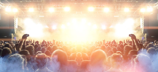 Front view of a concert stage with concert crowd silhouettes clapping and raising hands to the band...