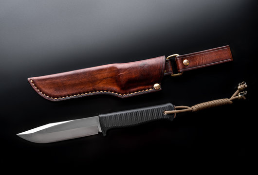 A modern hunting knife and a leather case for him on a dark background. Melee weapons for hunting and self-defense. The instrument of crime.