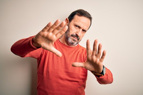 Middle age hoary man wearing casual orange sweater standing over isolated white background doing frame using hands palms and fingers, camera perspective