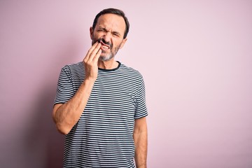 Middle age hoary man wearing casual striped t-shirt standing over isolated pink background touching mouth with hand with painful expression because of toothache or dental illness on teeth. Dentist