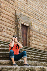 Young male traveler sitting on steps of an old town in Tuscany taking a photo on a vintage camera