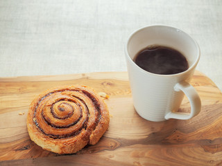 Fresh crispy cinnamon roll on a wooden surface and white cup with coffee. Pastry product.