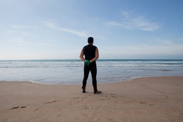 Swimmer in wetsuit on beach looking out over ocean 