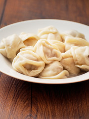 Portion of Russian traditional big size dumpling on a white plate and wooden table. Close up.
