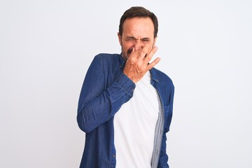 Fototapeta premium Middle age handsome man wearing blue denim shirt standing over isolated white background smelling something stinky and disgusting, intolerable smell, holding breath with fingers on nose. Bad smells
