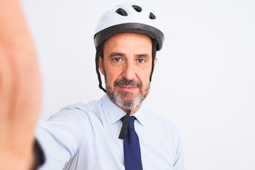 Middle age businessman wearing bike helmet make selfie over isolated white background with a confident expression on smart face thinking serious