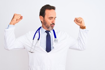 Middle age doctor man wearing coat and stethoscope standing over isolated white background showing arms muscles smiling proud. Fitness concept.