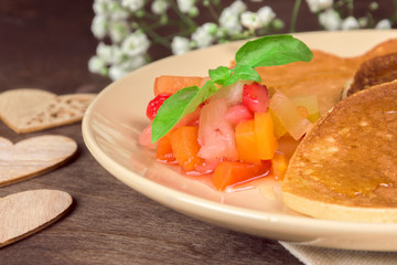 Colorful fruit chutney salad of exotic fruits and berries with a sprig of basil on a plate with homemade pancakes. Vitamin Healthy Breakfast Vegetarian Concept. Closeup