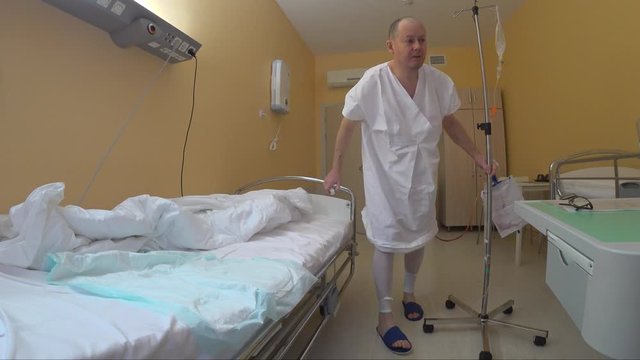 The patient goes to the toilet on his own after the operation. Crumpled bed with disposable diaper, hospital clothes, mobile drip rack moves patient with tubes of different colors.