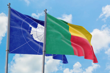 Benin and Antarctica flags waving in the wind against white cloudy blue sky together. Diplomacy concept, international relations.