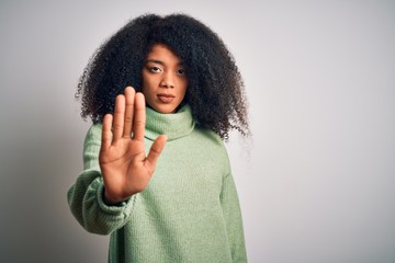 Young beautiful african american woman with afro hair wearing green winter sweater doing stop sing with palm of the hand. Warning expression with negative and serious gesture on the face.