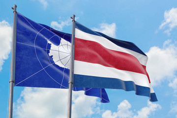 Costa Rica and Antarctica flags waving in the wind against white cloudy blue sky together. Diplomacy concept, international relations.
