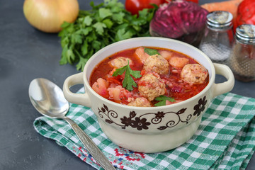 Soup with meatballs and vegetables in a bowl against a dark background