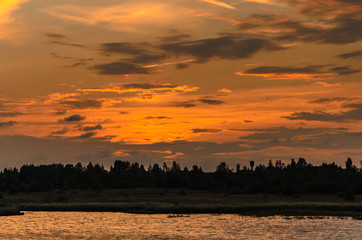 Sunlit clouds over the forest and river after sunset.