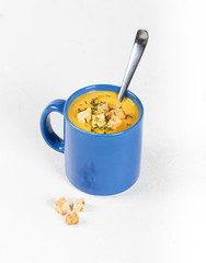 Pumpkin soup-puree with cream, wheat croutons and greens in a blue mug on a light background
