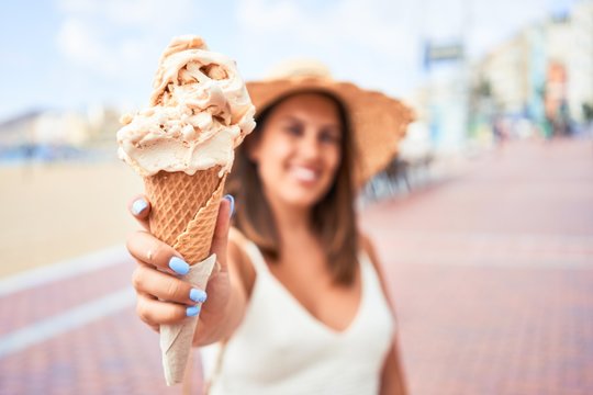 Young beautiful woman eating ice cream cone by the beach on a sunny day of summer on holidays
