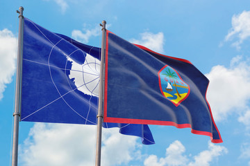Guam and Antarctica flags waving in the wind against white cloudy blue sky together. Diplomacy concept, international relations.