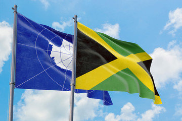 Jamaica and Antarctica flags waving in the wind against white cloudy blue sky together. Diplomacy concept, international relations.