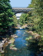 The Bridge at Tumwater Falls with trees and bushes shimmering in the water during summertime with a blue sky thurston county washington state.