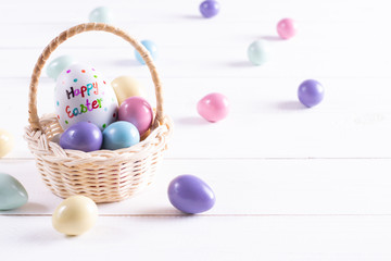 Easter basket filled with colorful eggs on white wooden background. Copy space.