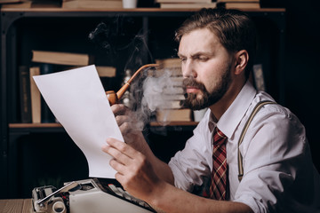 Stylish male writer with tie and braces smoking tobacco pipe and reading his text