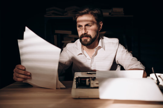 Pensive handsome bearded writer rereading his texts in a study lit by morning sun
