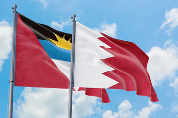 Bahrain and Antigua and Barbuda flags waving in the wind against white cloudy blue sky together. Diplomacy concept, international relations.