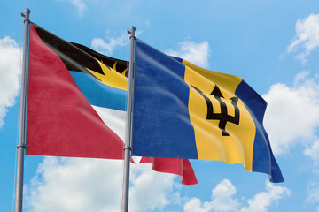 Barbados and Antigua and Barbuda flags waving in the wind against white cloudy blue sky together. Diplomacy concept, international relations.
