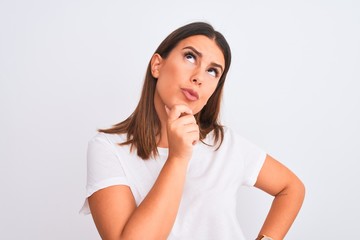 Portrait of beautiful and young brunette woman standing over isolated white background with hand on chin thinking about question, pensive expression. Smiling with thoughtful face. Doubt concept.