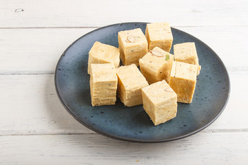 traditional indian candy soan papdi in a blue ceramic plate with almond and pistache on a white wooden background. side view