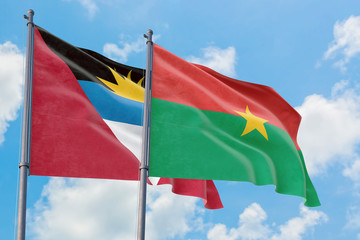Burkina Faso and Antigua and Barbuda flags waving in the wind against white cloudy blue sky together. Diplomacy concept, international relations.
