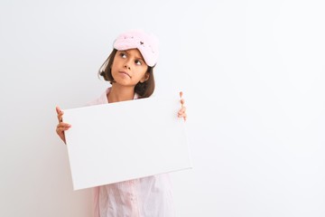 Child girl wearing sleep mask and pajama holding banner over isolated white background serious face thinking about question, very confused idea