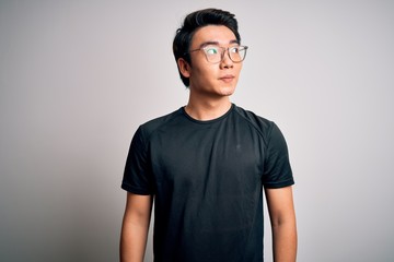 Young handsome chinese man wearing black t-shirt and glasses over white background smiling looking...